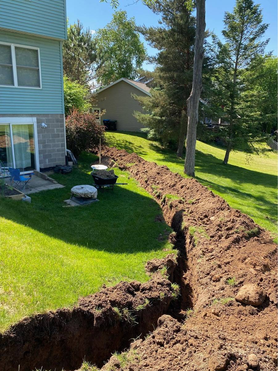 Narrow drainage trench dug across a residential backyard lawn