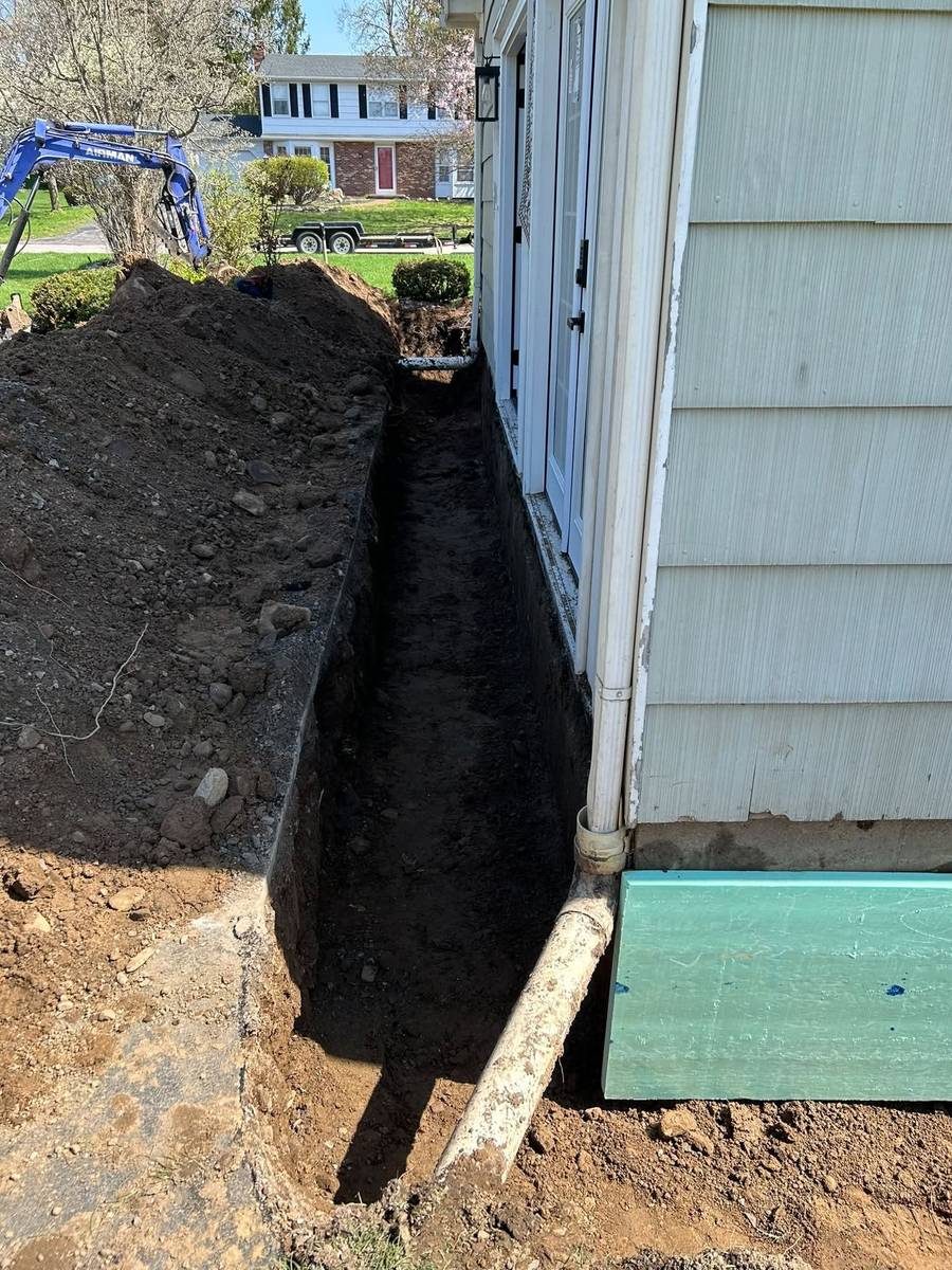 Trench excavated along a house foundation to run a new downspout drain line