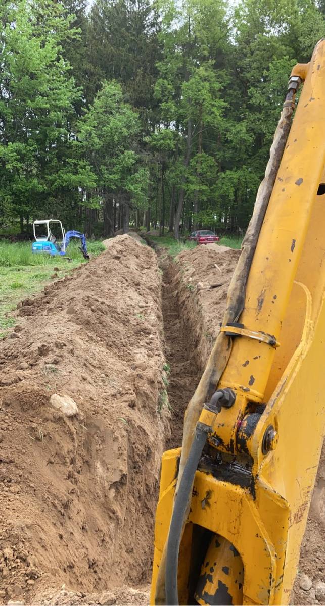 Utility trench dug in open ground with backhoe working and mini excavator staged behind